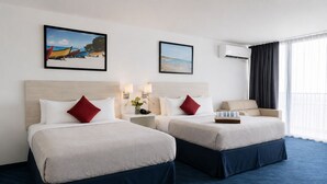 Hotelkamer met twee bedden, een bureau, een stoel, een nachtkastje, een lamp, een airconditioner en een raam met gordijnen.