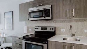 Een moderne keuken met een ingebouwde magnetron, oven en spoelbak, houten kastjes en een betegelde vloer.