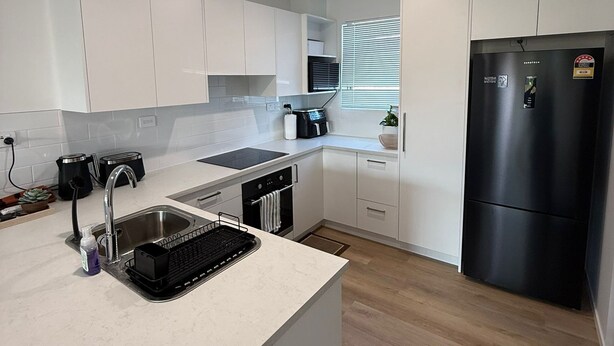 Una cocina moderna con armarios blancos, un lavamanos de acero inoxidable, un refrigerador negro y un microondas.