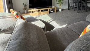 Una sala de estar moderna con un televisor de pantalla plana, sofás grises, un comedor con sillas y una planta en maceta.