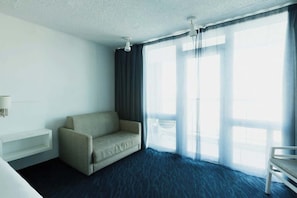 Ein Hotelzimmer mit einer Couch, einem Sessel, einem Nachttisch und einem großen Fenster mit Vorhängen.
