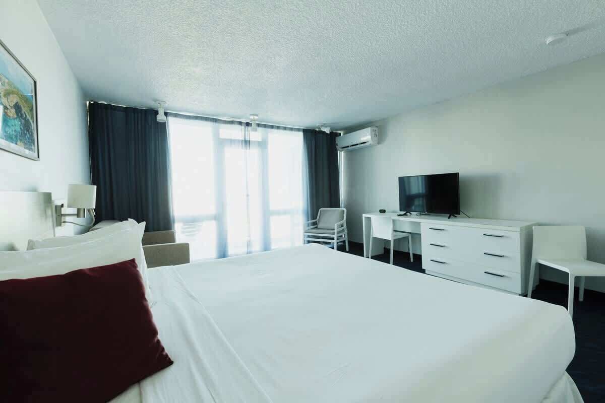 Habitación de hotel con cama, escritorio, silla, televisor y ventana con cortinas.