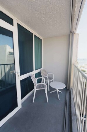 Ein Balkon mit zwei weißen Stühlen, einem kleinen runden Tisch, einer Schiebeglastür und Blick aufs Meer.
