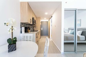 Eine moderne Küche mit Holdekor und einer weißen Arbeitsplatte, ein Essbereich mit einem weißen Tisch und ein Schlafzimmer mit einem Bett und einer Glasschiebetür.