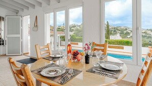 A dining area with a round table, chairs, and a view of a swimming pool and landscape.