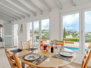 Ein Essbereich mit rundem Tisch, Stühlen und Blick auf Pool und Landschaft.