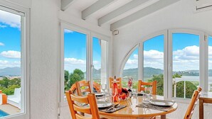 A dining area with a round table, wooden chairs, and a view of the landscape through large windows.