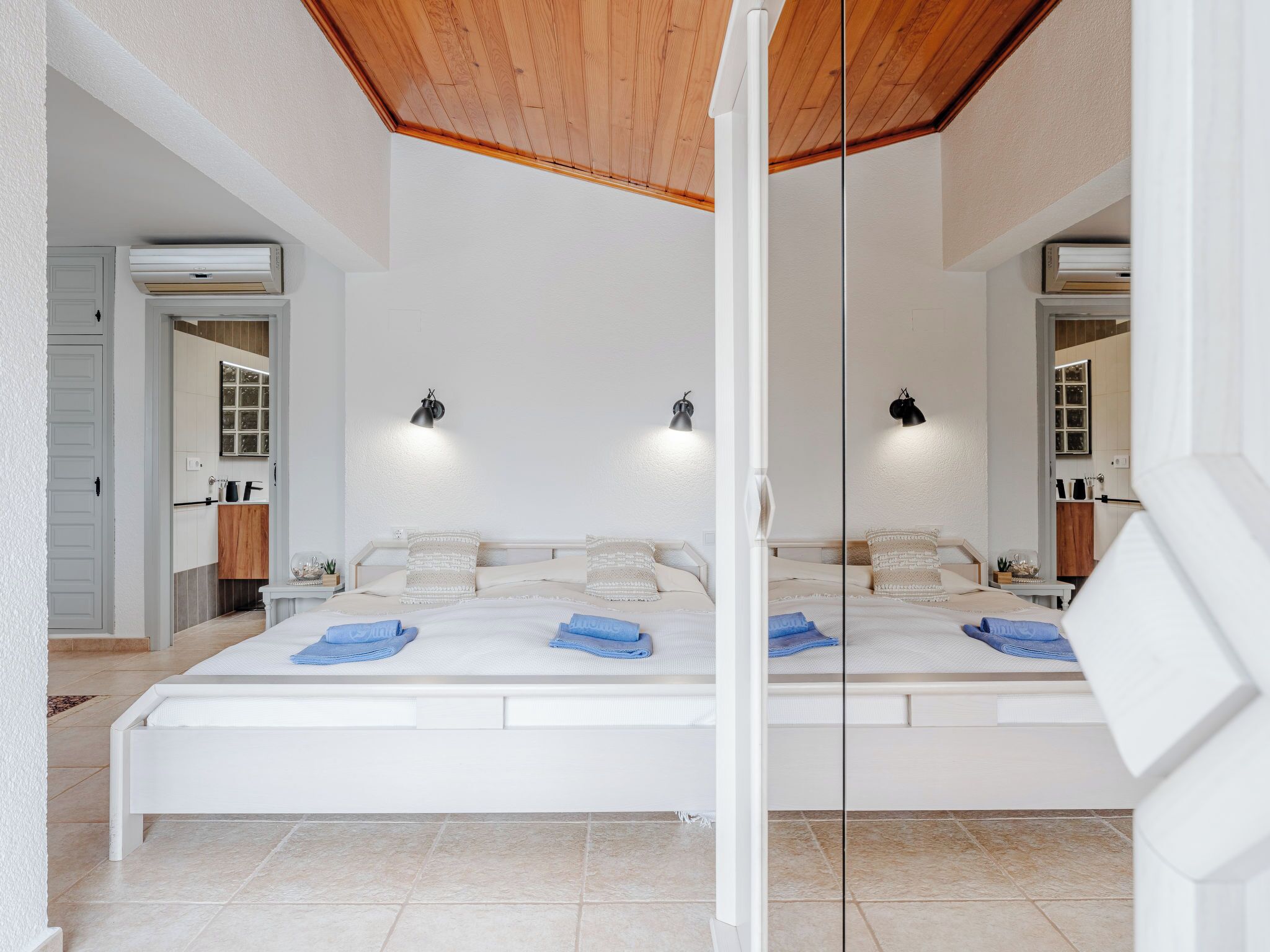 A large bed with a wooden ceiling, white walls, and two bedside lamps.