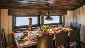 Une table à manger en bois, des chaises, un luminaire suspendu et une fenêtre donnant sur un beau paysage.