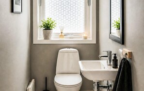 A bathroom with a toilet, sink, window, and potted plants.
