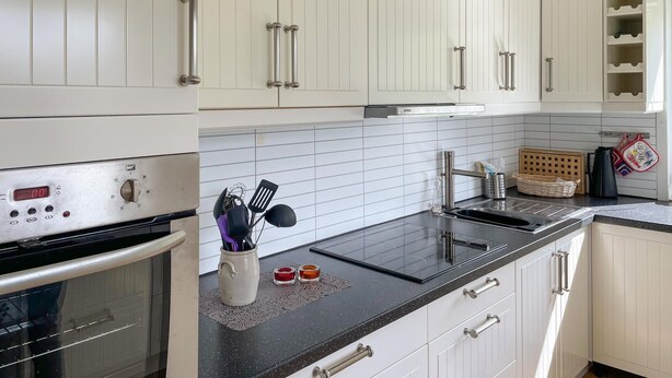 Una cucina con mobili bianchi, un piano di lavoro nero e elettrodomestici in acciaio inossidabile.
