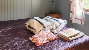 Un letto con copripiumino viola, due cuscini con la scritta 'hoie', un cuscino a motivi rossi e una pila di libri.