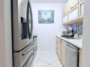 Eine kompakte Küche mit Kühlschrank, Backofen, Geschirrspüler und Spüle mit Armatur.