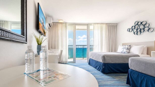 Ein Hotelzimmer mit Bett, Schreibtisch, Stuhl, Tisch mit Wasserflaschen und Blick aufs Meer.