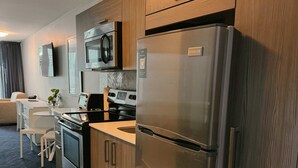 A modern kitchen with stainless steel appliances, wooden cabinets, a flat-screen TV, and a dining area with a white table and chairs. - Beachfront Isla Verde Studio withPrivate Balcony (Carolina)