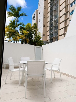 A rooftop patio with white plastic chairs and a table, surrounded by a white wall and a building with balconies. - Beachfront Isla Verde Studio withPrivate Balcony (Carolina)