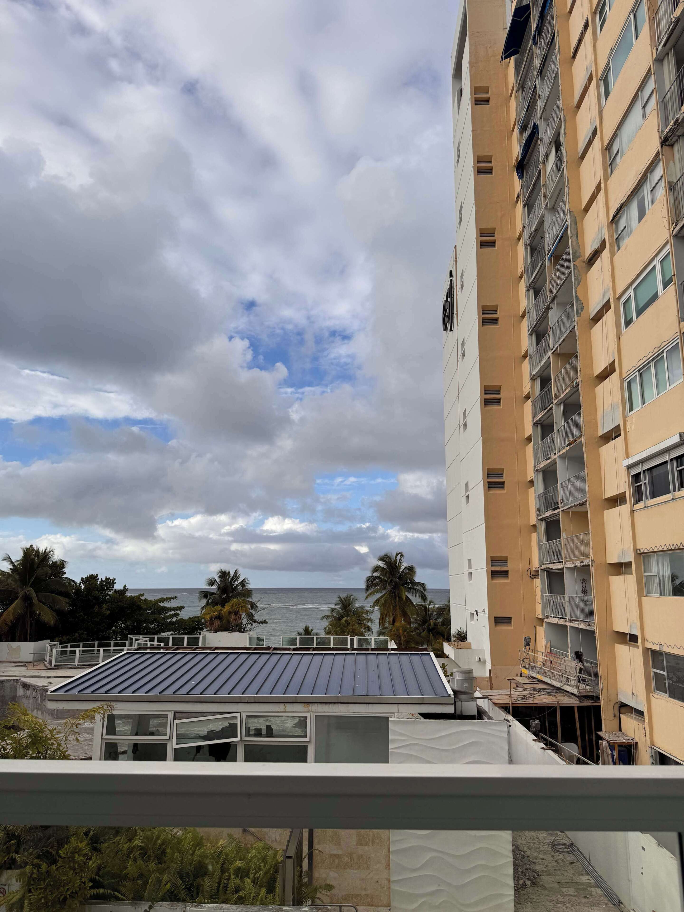 A high-rise building with multiple balconies, a view of the ocean, and palm trees.