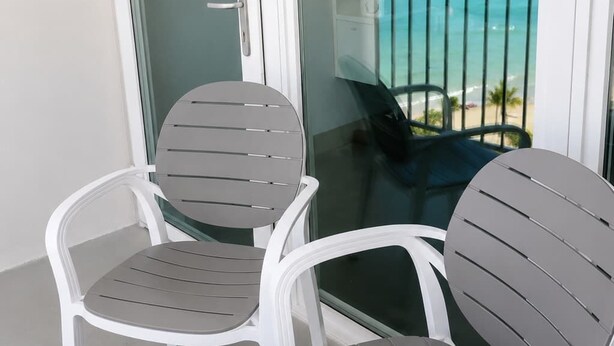 A balcony with two chairs and a table, overlooking a beach and ocean. - Romantic Ocean View Penthouse - King Bed - Balcony (Carolina)