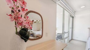 Ein Zimmer mit einem Holztisch, einer weißen Vase mit rosa Blumen und einem Spiegel an der Wand.