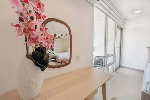 Ein Zimmer mit einem Holztisch, einer weißen Vase mit rosa Blumen und einem Spiegel an der Wand.