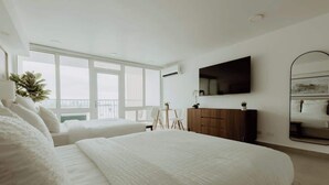 A modern bedroom with a large bed, a flat-screen TV, a mirror, and a balcony with a view. - Elegant Studio with Ocean Views - Isla Verde Beach (Carolina)
