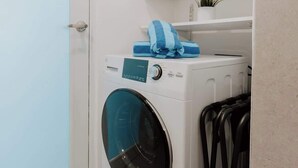 A compact laundry room with a front-loading washing machine, a drying rack, and a small shelf with a plant. - Elegant Studio with Ocean Views - Isla Verde Beach (Carolina)