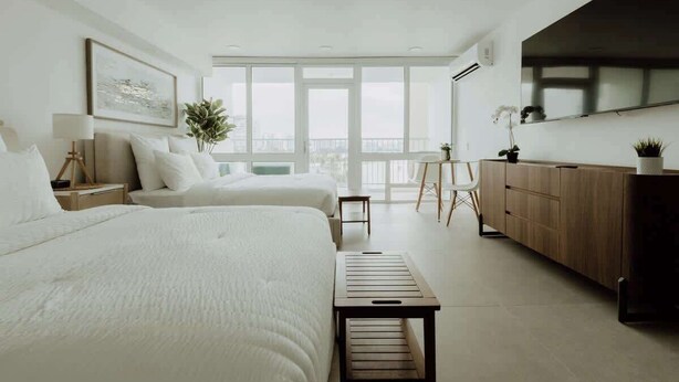 A modern hotel room with two beds, a large window, a TV, and a balcony. - Elegant Studio with Ocean Views - Isla Verde Beach (Carolina)