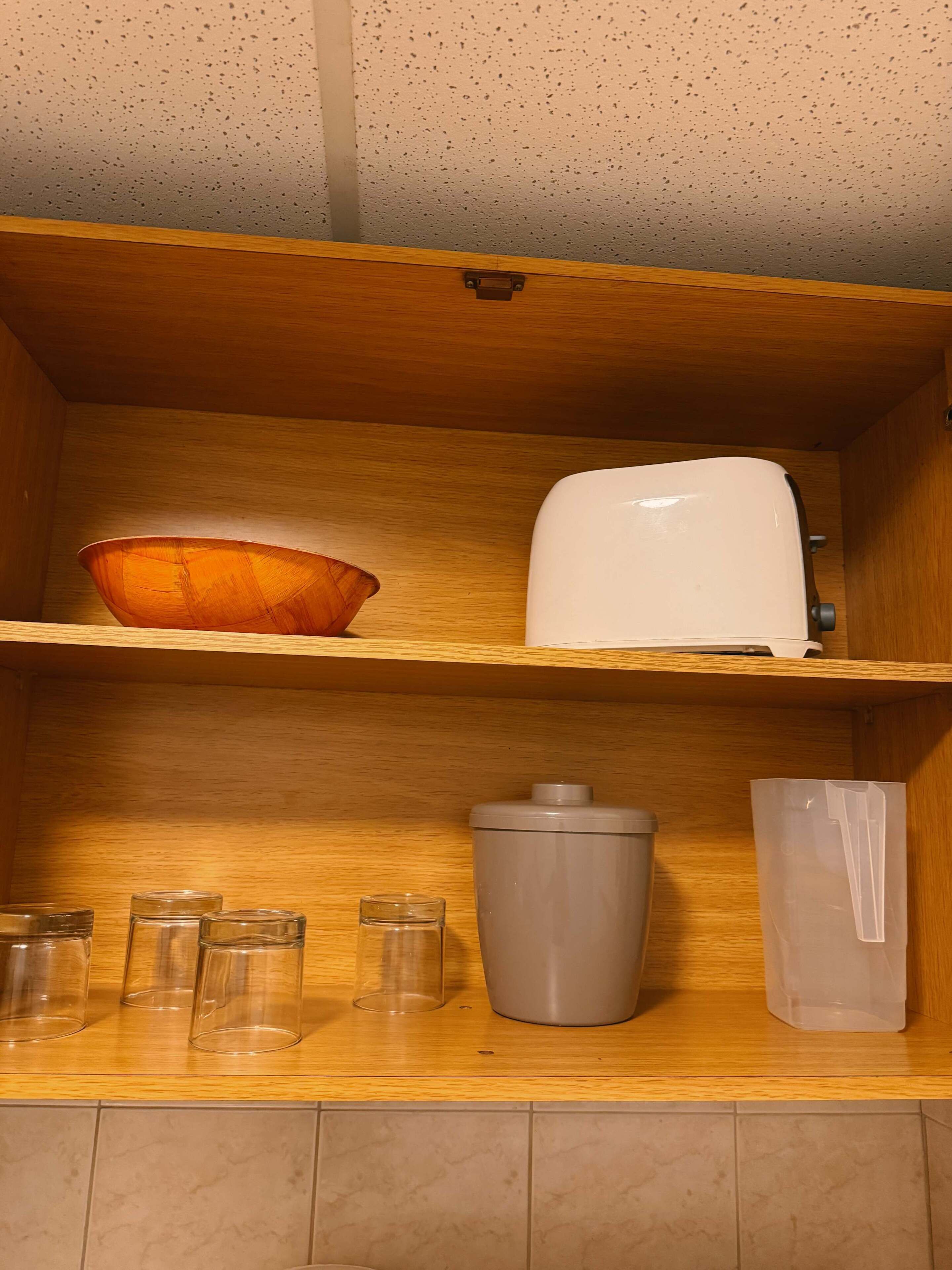 Une étagère de cuisine avec un saladier en bois, un appareil électroménager blanc, plusieurs bocaux en verre, un récipient gris et un sac en plastique.