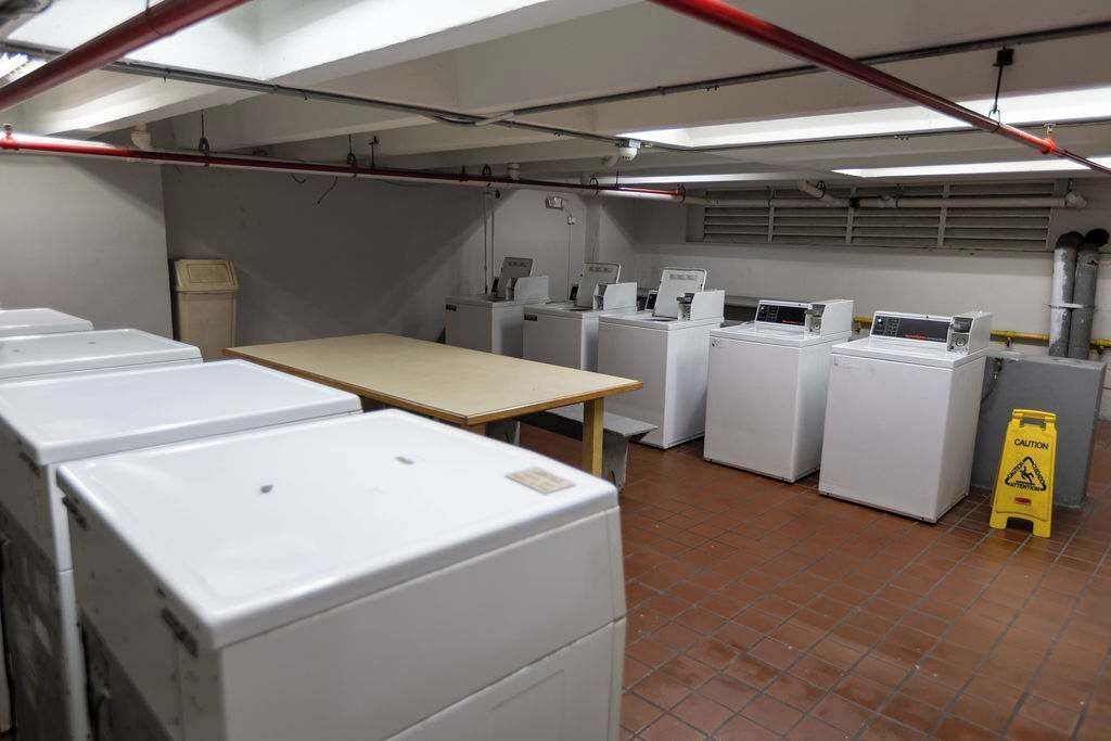 Une buanderie équipée de plusieurs machines à laver, d’une table et de panneaux d’avertissement.