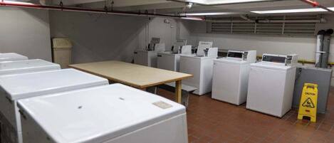Une buanderie équipée de plusieurs machines à laver, d’une table et de panneaux d’avertissement.