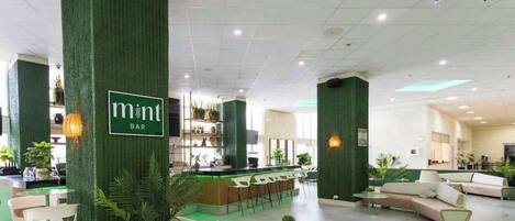 A modern bar area with green accent walls, a reception desk, and seating arrangements.