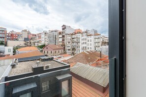 A cityscape with a mix of modern and traditional buildings, a clear sky, and a view through a window with a metal frame. - GuestReady - Studio in the heart of Porto (Porto)