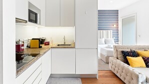 Eine kompakte Küche mit Spüle, Herd und Mikrowelle, ein kleiner Essbereich und ein Schlafzimmer mit Bett und Schlafsofa.