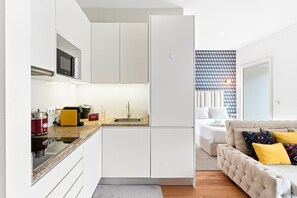 A compact kitchen with a sink, stove, and microwave, a small dining area, and a bedroom with a bed and sofa. - GuestReady - Studio in the heart of Porto (Porto)