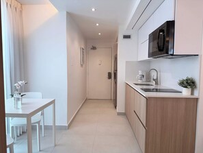 A modern kitchen with a microwave, coffee maker, and a potted plant. There is a dining area with a table and chairs. - Balcony Studio - Ocean Breezes, AC- Prime Location (Carolina)