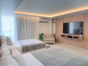 A modern hotel room with a large flat-screen TV, a sofa, a chair, and a bed. - Balcony Studio - Ocean Breezes, AC- Prime Location (Carolina)