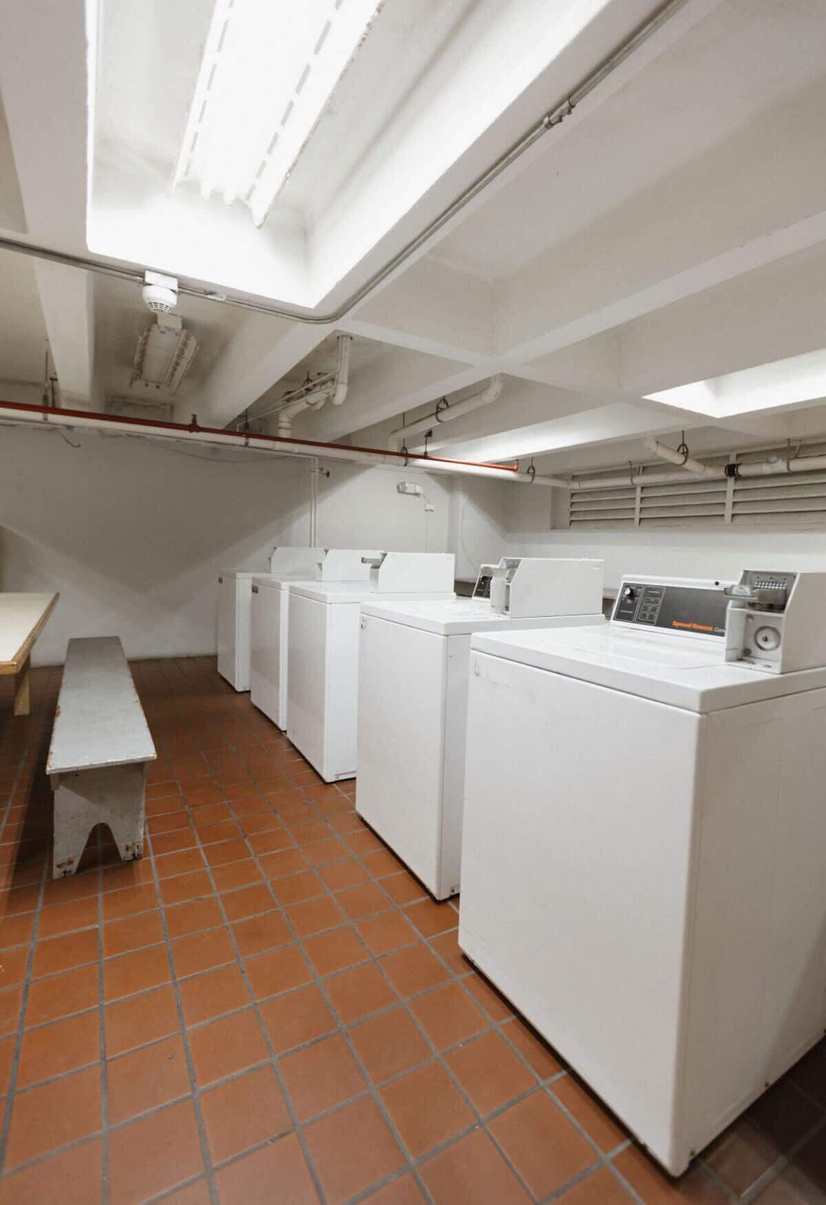 A laundry room with four white washing machines, a bench, and a tiled floor.