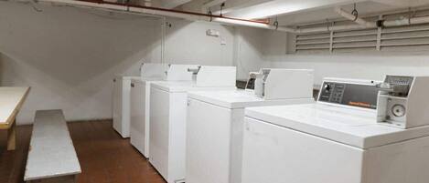 A laundry room with four white washing machines, a bench, and a tiled floor.