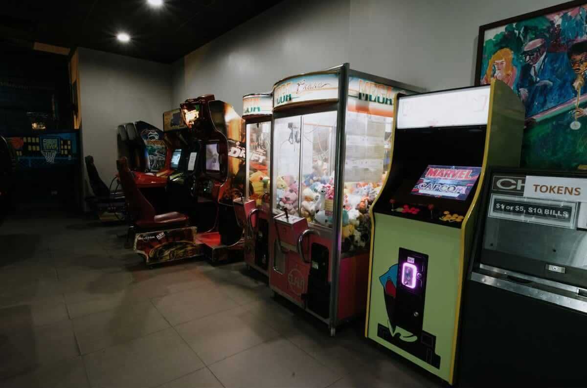 A row of arcade machines with tokens and bills, and a wall with a poster.