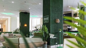 Ein modernes Interieur mit grünen, strukturierten Wänden, einer Bar, Sitzgelegenheiten und einer Rezeption.
