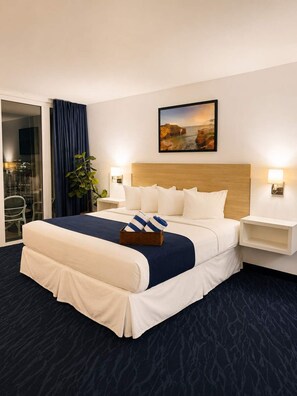 Ein Hotelzimmer mit einem großen Bett, einem Nachttisch, einer Wandlampe, einer Zimmerpflanze und einem Gemälde.