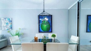 Un'area pranzo moderna con tavolo in vetro, sedie bianche, lampadario e opere d'arte alle pareti.