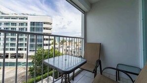Un balcone con tavolo e sedie in vetro, affacciato su un'area parcheggio e edifici.