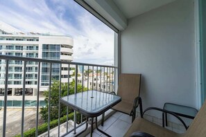 A balcony with a glass table and chairs, overlooking a parking area and buildings. - 2BR w/King + 3 Twins • Balcony • on the Beach (Carolina)
