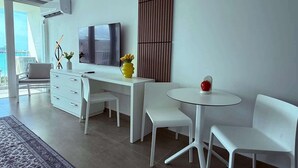 Una habitación de hotel moderna con un escritorio blanco, dos sillas, una mesa redonda, un televisor y un ventanal grande.