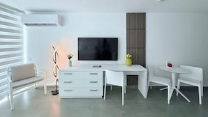 Una sala de estar moderna con un televisor de pantalla plana, muebles blancos, un jarrón decorativo y un aire acondicionado instalado en la pared.