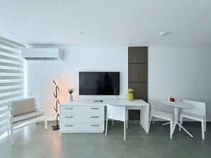 A modern living room with a flat-screen TV, white furniture, a decorative vase, and a wall-mounted air conditioner. - Stylish Oceanview Studio • 2Q Bed • Prime Location (Carolina)