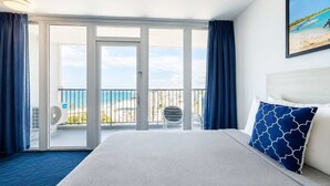 Ett hotellrum med en säng, utsikt över stranden och en balkong med en stol.