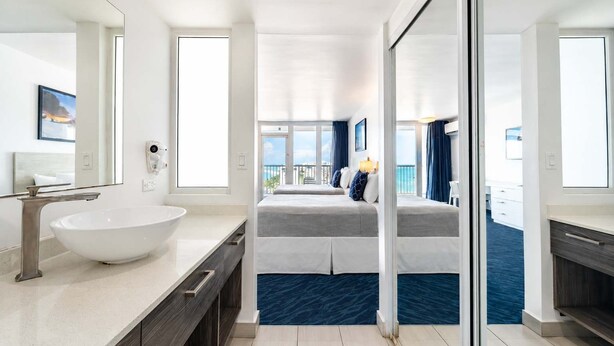 Ett modernt hotellrum med en stor säng, ett vitt handfat och en balkong med utsikt över havet.