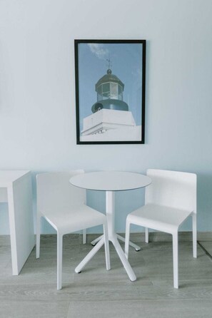 Ein gerahmtes Bild eines Leuchtturms an einer Wand, ein runder weißer Tisch mit zwei Stühlen und eine hellblaue Wand.